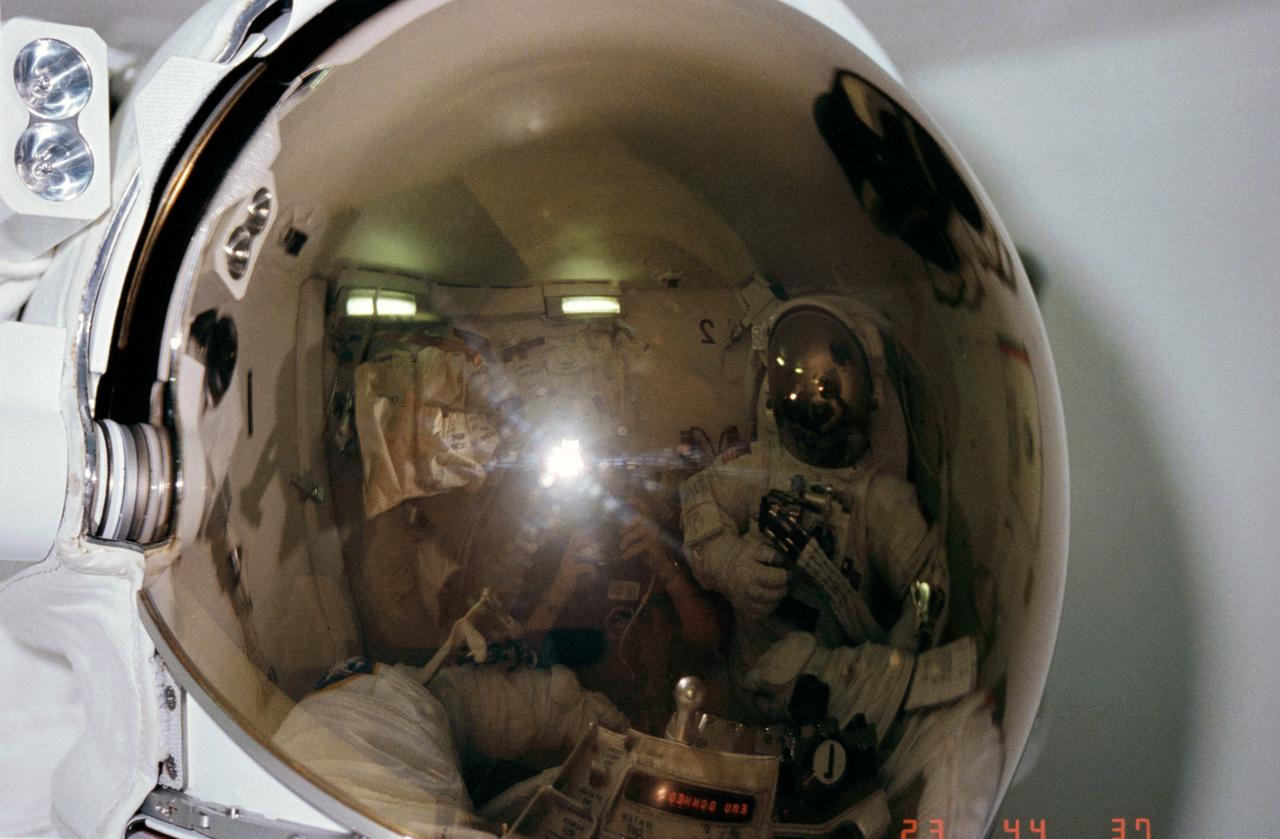 STS006-06-465 (7 April 1983) --- Three-fourths of the STS-6 astronaut crew appears in this unusual 35mm frame exposed in the airlock of the Earth-orbiting space shuttle Challenger. Astronaut F. Story Musgrave’s helmet visor encompasses all the action in the frame. Dr. Musgrave and astronaut Donald H. Peterson (reflected on right side of the visor) were fully suited in their Extravehicular Mobility Unit (EMU) spacesuits and were participating in EVA preparation exercises. Astronaut Karol J. Bobko, STS-6 pilot, wearing conventional onboard shuttle clothing, photographed the two during their procedures and appears at center of frame. The reversed number (1 and 2 in the mirrored image represent the EVA designations for the two mission specialists. Photo credit: NASA
