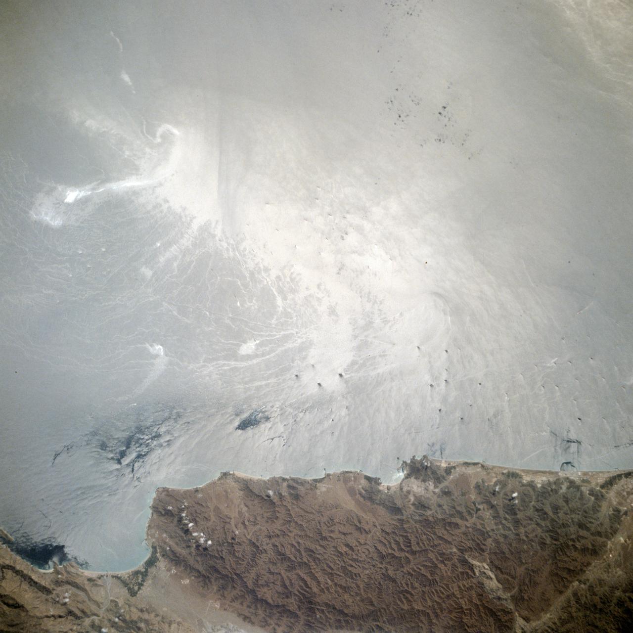 STS006-44-532 (4-9 April 1983) --- This is one of a series of photographs taken through the “ceiling” windows of the Earth-orbiting space shuttle Challenger by members of the STS-6 crew on its five-day mission in space. Many unused oil tankers lie in the roadstead along the coast of U.A.E. between the ports of Khawn Fakkan and Fujayrah. The sunglint on the Gulf of Oman permits the viewer to see the surface features much clearer. Such surface features as gynes, slicks, wakes, and sea state are clearly seen. Photo credit: NASA