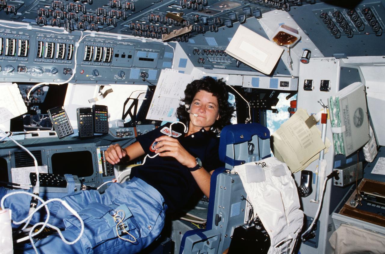 STS007-14-629 (21 June 1983) --– Astronaut Sally K. Ride, STS-7 mission specialist, performs a number of functions simultaneously, proving the necessity for versatility and dexterity in space travel. Floating freely on the flight deck, Dr. Ride communicates with ground controllers in Houston, moves within feet of important reference data, hand calculators and other aids all at the same time. She is one of the five astronaut crew members for the Challenger’s second orbital mission. Her head is in the station normally occupied by the pilot (in this case, Frederick H. (Rick) Hauck) and her feet are anchored at the station for the crew commander (in this case, Robert L. Crippen). Photo credit: NASA