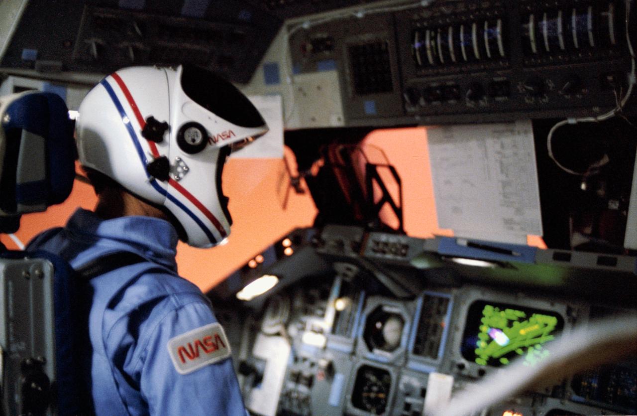 STS007-31-1614 & S83-35775 (24 June 1983) ---   Astronaut Robert L. Crippen is seen at the commander’s station of the Space Shuttle Challenger as it passes through the Earth’s atmosphere on re-entry.  The friction results in a pinkish glow visible through the forward windows on the flight deck.  The scene was exposed with a 35mm camera.  