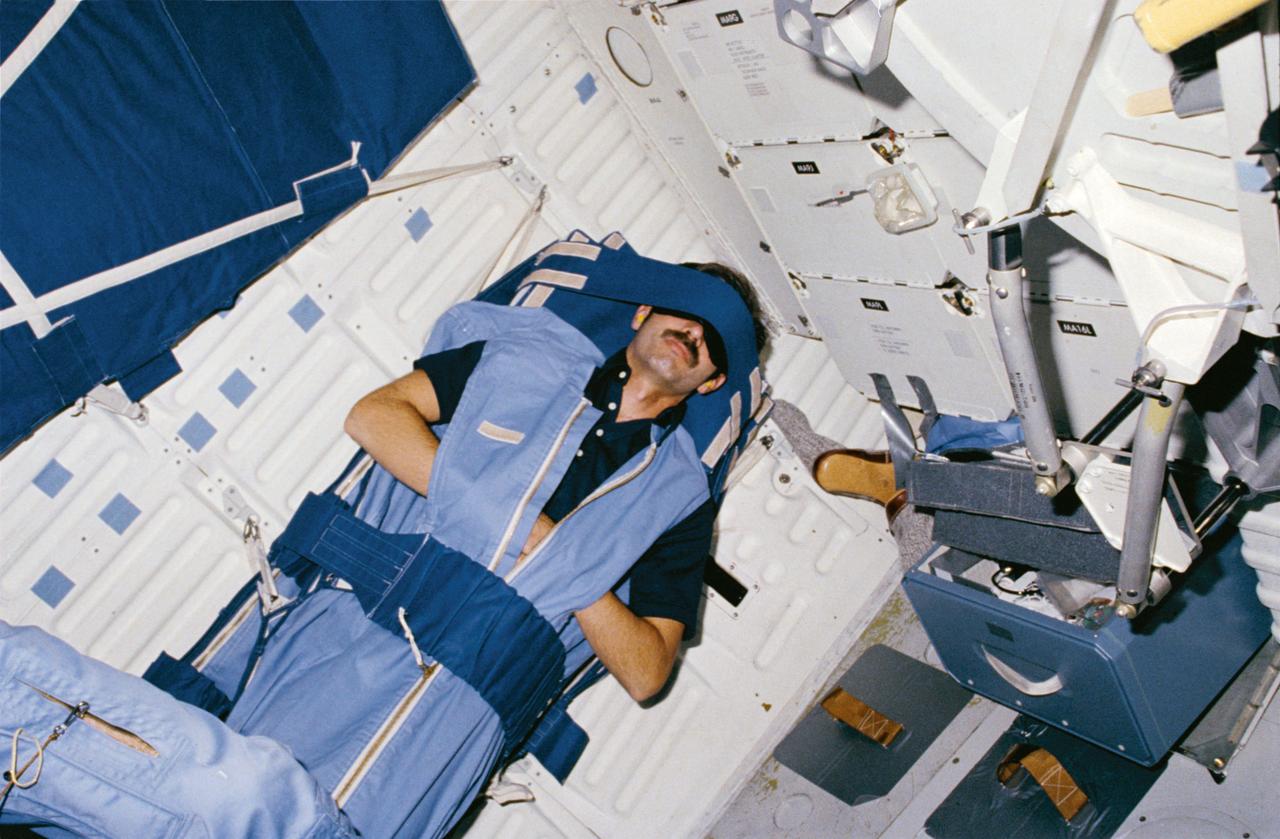 STS008-05-145 (5 Sept 1983) --- On middeck (MDK), Mission Specialist (MS) Gardner sleeps in sleep restraint attached to starboard wall.  Open airlock hatch, airlock hatch hinge, and free-floating footwear appear in view.