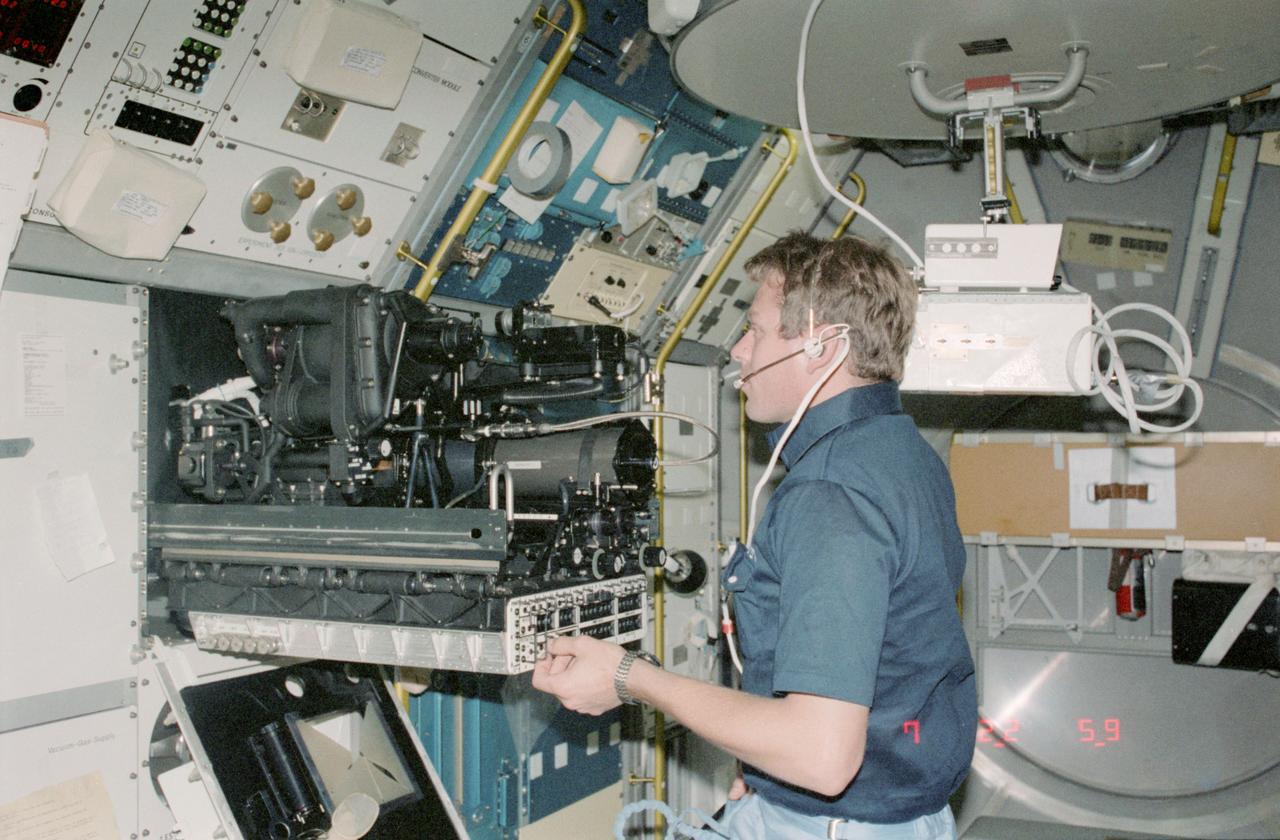 STS009-125-427 (28 Nov 1983) --- Payload Specialist Byron K. Lichtenberg carries out an experiment at the fluid physics module on the busy materials science double rack facility. Two beverage containers can be seen just above the biomedical engineer's head.
