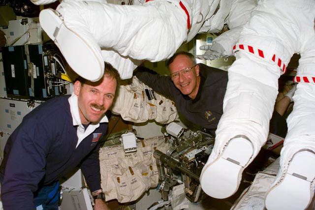 S103-E-5023 (20 December 1999) ---  Astronauts Steven L. Smith (foreground) and Claude Nicollier take an early look at their extravehicular mobility unit (EMU) space suits on Discovery's mid deck near the end of their first full day in space.  Smith is payload commander and Nicollier, mission specialist representing the European Space Agency (ESA).  The two will participate in space walks to service the Hubble Space Telescope later in the week. The photo was recorded with an electronic still camera (ESC) at 21:52.32 GMT, December 20, 1999.
