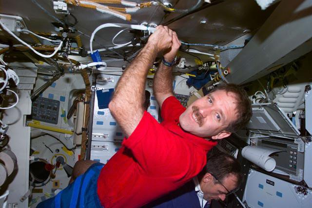 S103-E-5197 (21 Dec. 1998) --- Astronaut John M. Grunsfeld, mission specialist,  checks a cable connection on Discovery's mid deck during Flight Day 2 activity.  Astronaut Steven L. Smith, payload commander, is partially visible in the  electronic still camera's (ESC) frame, recorded at 11:10:22 GMT, Dec. 21, 1999.
