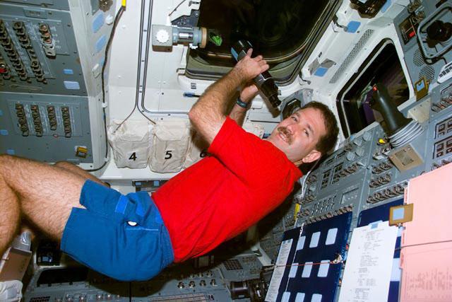 S103-E-5202 (21 Dec. 1999) --- Astronaut John M. Grunsfeld, uses a pair of binoculars to view the distant Hubble Space Telescope (HST) several hours prior to its capture by the Space Shuttle Discovery. The photo was taken with an electronic still camera (ESC) at  12:45.30 GMT, Dec. 21, 1999.