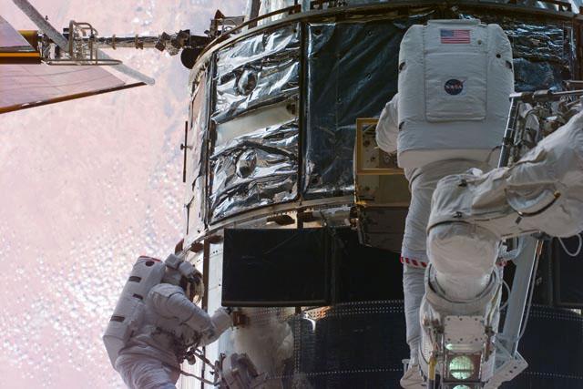 S103-E-5320 (23 December 1999) --- Astronauts C. Michael Foale (left) and  Claude Nicollier work on the Hubble Space Telescope (HST)in Discovery's aft cargo bay during their shared space walk to perform servicing tasks on the  Hubble Space Telescope (HST). A desert area on Earth forms the backdrop for the photo.  Nicollier, part of the astronaut corps since 1980, represents the European Space Agency (ESA).  Foale, one of NASA's astronauts who had spent several months aboard Russia's Mir Space Station, is an alumnus of the 1987 class of astronaut candidates.  The photo was taken with an electronic still camera (ESC).