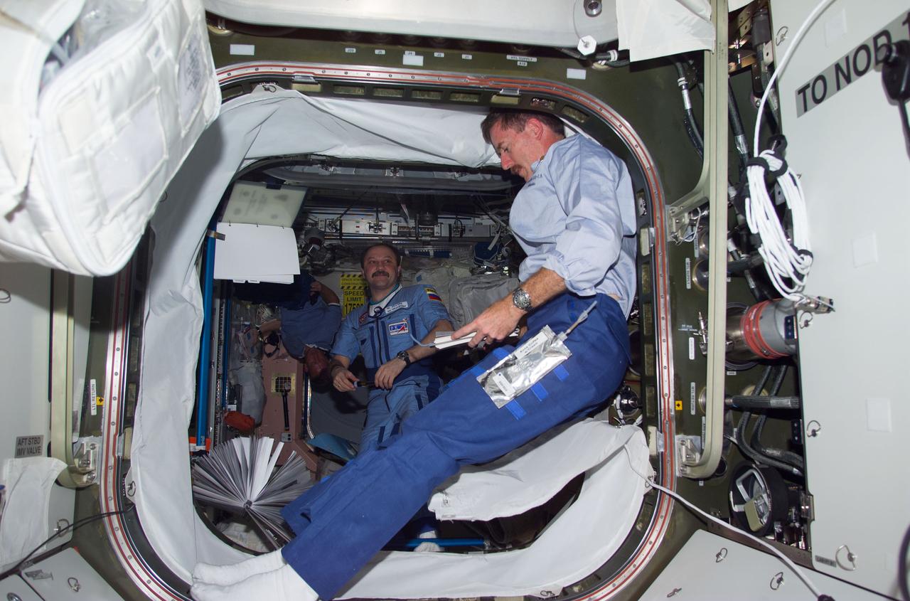 S104-E-5108 (16 July 2001) --- James F. Reilly, STS-104 mission specialist, reads over a checklist in the hatchway of the newly installed Quest Airlock.  In the background, cosmonaut Yury V. Usachev of Rosaviakosmos, Expedition Two mission commander, is working in Unity Node 1.