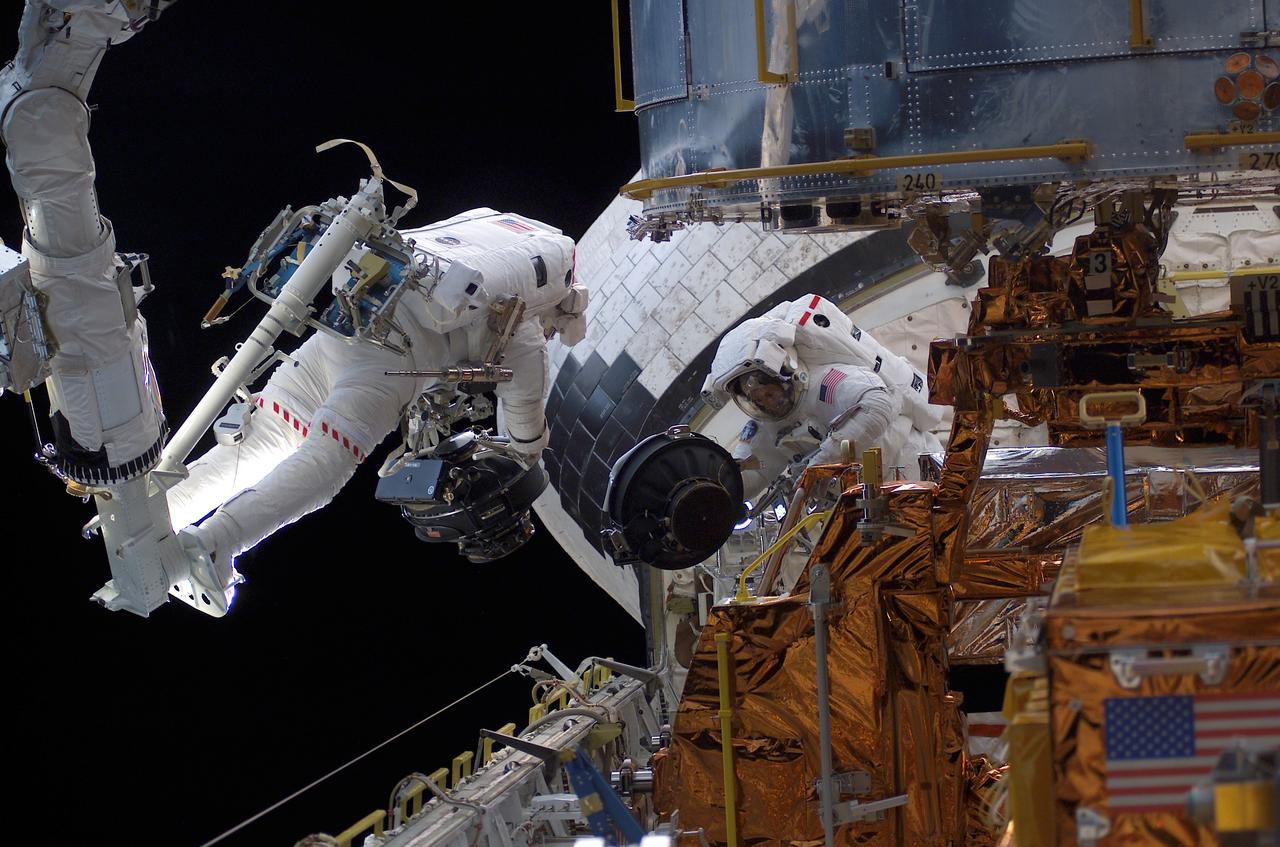 STS109-E-5402 (5 March 2002) --- With his feet secured on a platform connected to the remote manipulator system (RMS) robotic arm of the Space Shuttle Columbia, astronaut Michael J. Massimino, mission specialist, hovers over the shuttle's cargo bay while working in tandem with astronaut James H. Newman, mission specialist, during the STS-109 mission's second day of extravehicular activity (EVA). Inside Columbia's cabin, astronaut Nancy J. Currie, mission specialist, controlled the RMS.  The image was recorded with a digital still camera.