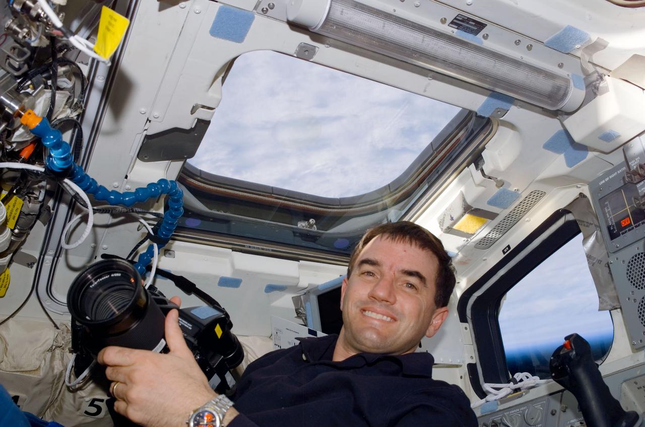 STS110-E-5017 (8 April 2002) --- Astronaut Rex J. Walheim, STS-110 mission specialist, holds a camera on the aft flight deck of the Space Shuttle Atlantis. A blue and white Earth is visible through the overhead windows of the orbiter. The image was taken with a digital still camera.