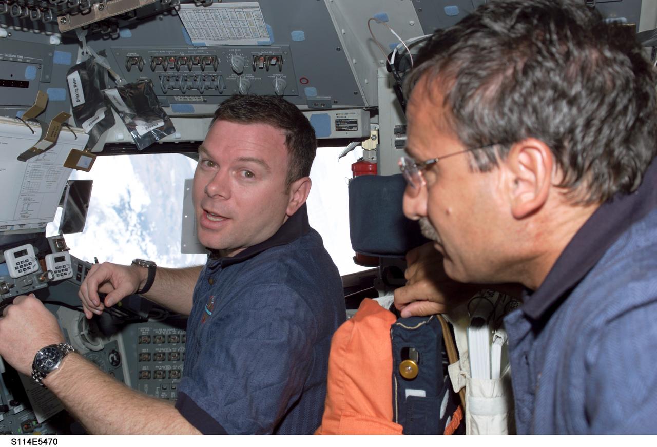 STS114-E-05470 (28 July 2005) --- Astronauts James M. Kelly, left, at pilot's station on Discovery, looks toward the aft cabin area during rendezvous and docking operations with International Space Station (ISS).