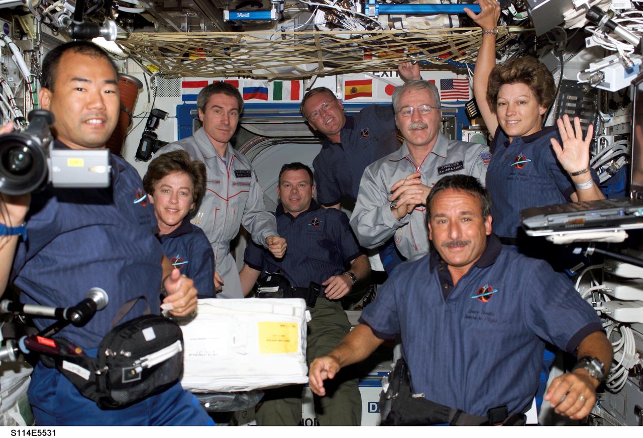 S114-E-5531 (28 July 2005) --- Not since 2002 have nine space travelers shared space simultaneously on the International Space Station. At least not until the morning of July 28, when astronaut Eileen M. Collins led her Discovery crew onboard the orbital outpost. Collins gives a wave from upper right. Clockwise from her position are astronaut Charles J. Camarda, Japanese Aerospace Agency astronaut Soichi Noguchi and Wendy Lawrence, all STS-114 mission specialists; cosmonaut Sergei Krikalev, Expedition 11 commander; astronaut James M. Kelly, Discovery pilot; astronaut Andrew S.W. Thomas, STS-114 mission specialist; and astronaut John L. Phillips, NASA Space Station Science Officer and flight engineer for Expedition 11. Astronaut Stephen K. Robinson, STS-114 mission specialist, took the photo with a digital still camera.