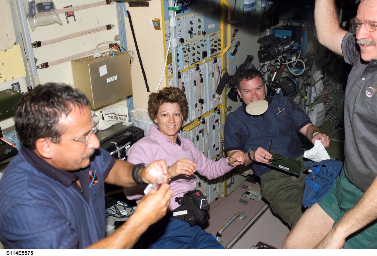 S114-E-5575 (28 July 2005) --- Astronaut John L. Phillips (right edge of frame), NASA Space Station science officer and flight engineer for Expedition 11,  serves as obliging co-host for members of the STS-114 crew during their first shared meal onboard the orbiting outpost. From the left are astronauts Charles J. Camarda, mission specialist; Eileen M. Collins, commander; and James M. Kelly, pilot. Kelly, like many astronauts before him, has discovered that a tortilla makes for better  sandwich-building than other type breads which are prone to creating troublesome crumbs in the weightless environment.