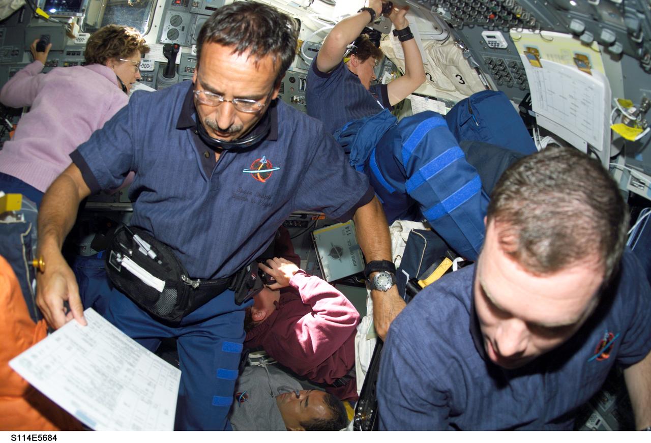 S114-E-5684 (28 July 2005) --- Astronauts Charles J. Camarda, STS-114 mission specialist, and James M. Kelly (right), pilot, assist with rendezvous and docking operations on the flight deck of the Space Shuttle Discovery, while surrounded by busy crewmates in this fish-eye scene captured by a digital still camera. Astronaut Eileen M. Collins, STS-114 commander, is temporarily on the aft flight deck in upper left frame. Also pictured are astronauts Stephen K. Robinson and Wendy Lawrence and Japanese Aerospace Agency astronaut Soichi Noguchi, all mission specialists.