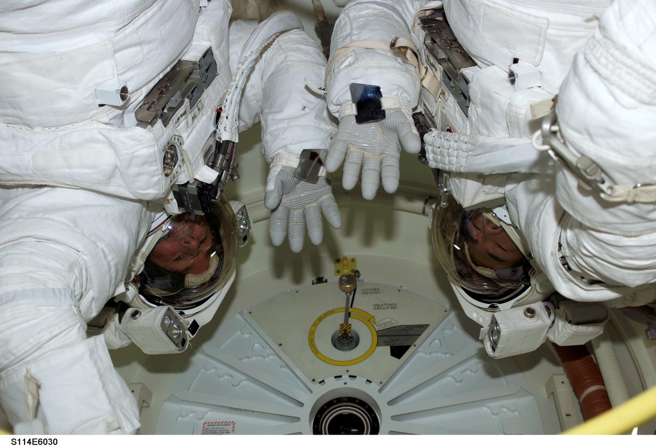 S114-E-6030 (1 August 2005) --- Astronaut Stephen K. Robinson (left) and Japan Aerospace Exploration Agency (JAXA) astronaut Soichi Noguchi, STS-114 mission specialists, wave as they prepare to egress Space Shuttle Discovery’s airlock for a seven-hour spacewalk to perform work on the International Space Station. Robinson and Noguchi are wearing their Extravehicular Mobility Unit (EMU) space suits.