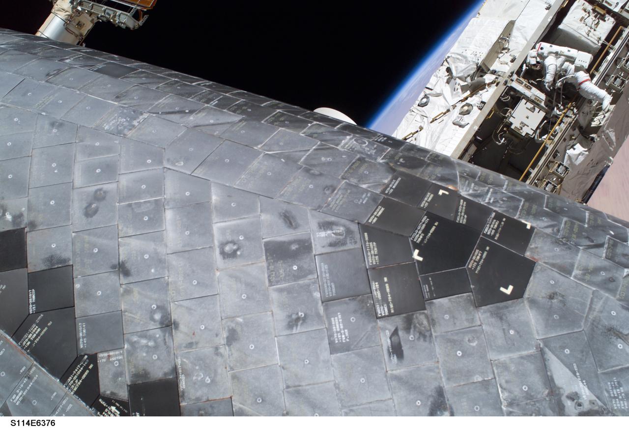 S114-E-6376 (3 August 2005) --- A close-up view of a portion of the thermal protection tiles on Space Shuttle Discovery&#0146;s underside is featured in this image photographed by astronaut Stephen K. Robinson (out of frame), STS-114 mission specialist, during the mission&#0146;s third session of extravehicular activities (EVA). While perched on a Space Station truss, astronaut Soichi Noguchi (background), mission specialist representing Japan Aerospace Exploration Agency (JAXA), acts as observer and communication relay station between fellow spacewalker Robinson and astronaut Andrew S. W. Thomas aboard Discovery.