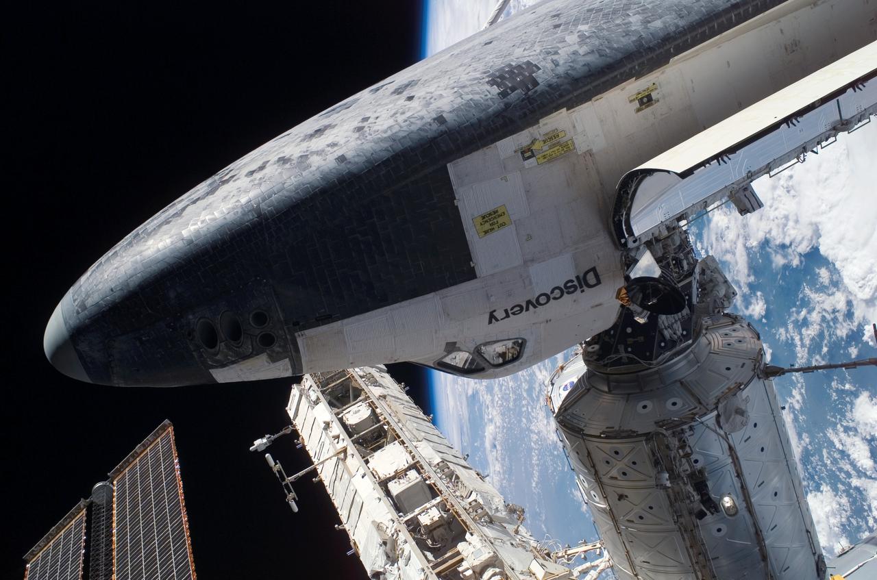 S114-E-6452 (3 August 2005) --- The Space Shuttle Discovery, docked to the Destiny laboratory of International Space Station, is featured in this image photographed by astronaut Stephen K. Robinson (out of frame), STS-114 mission specialist, during today;s spacewalk. Astronaut Soichi Noguchi, mission specialist representing Japan Aerospace Exploration Agency (JAXA), is partially visible between Discovery;s payload bay and Destiny. The blackness of space and Earth;s horizon formed the backdrop for the image.