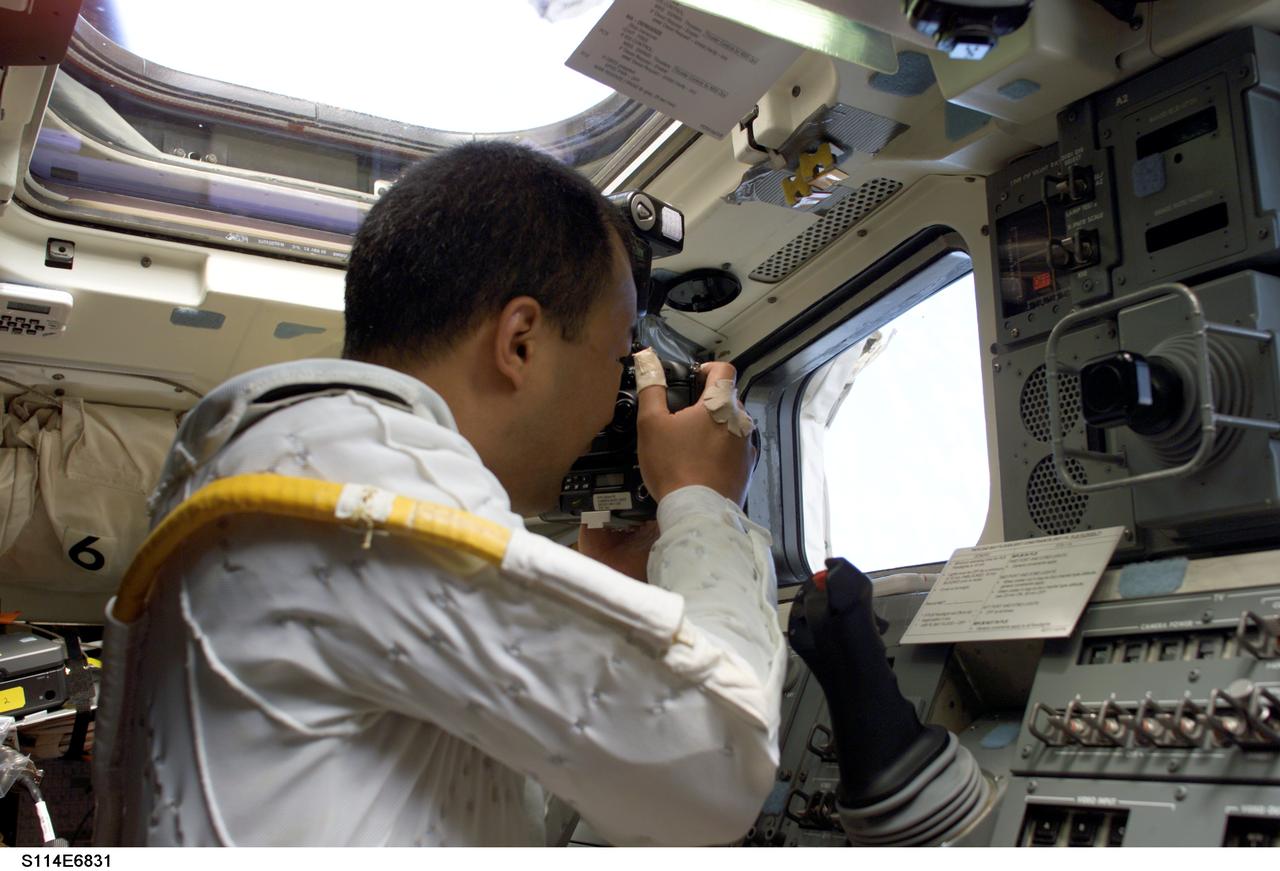 S114-E-6831 (3 August 2005) --- Astronaut Soichi Noguchi, STS-114 mission specialist representing Japan Aerospace Exploration Agency (JAXA), uses a still camera through an aft cabin cargo interface window on the Space Shuttle Discovery.