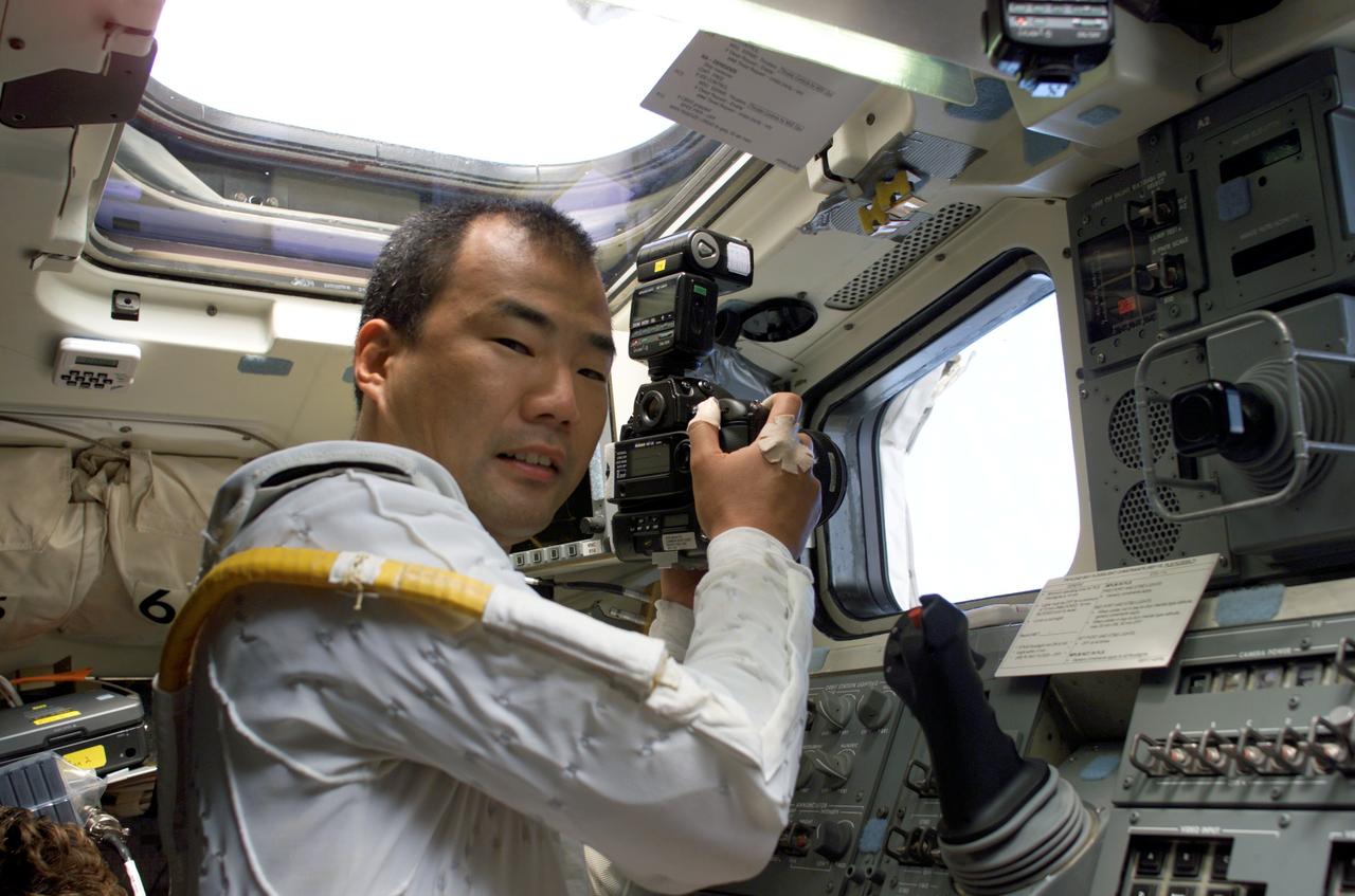 S114-E-6832 (3 August 2005) --- Astronaut Soichi Noguchi, STS-114 mission specialist representing the Japan Aerospace Exploration Agency (JAXA), uses a still camera through an aft cabin cargo interface window on the Space Shuttle Discovery.