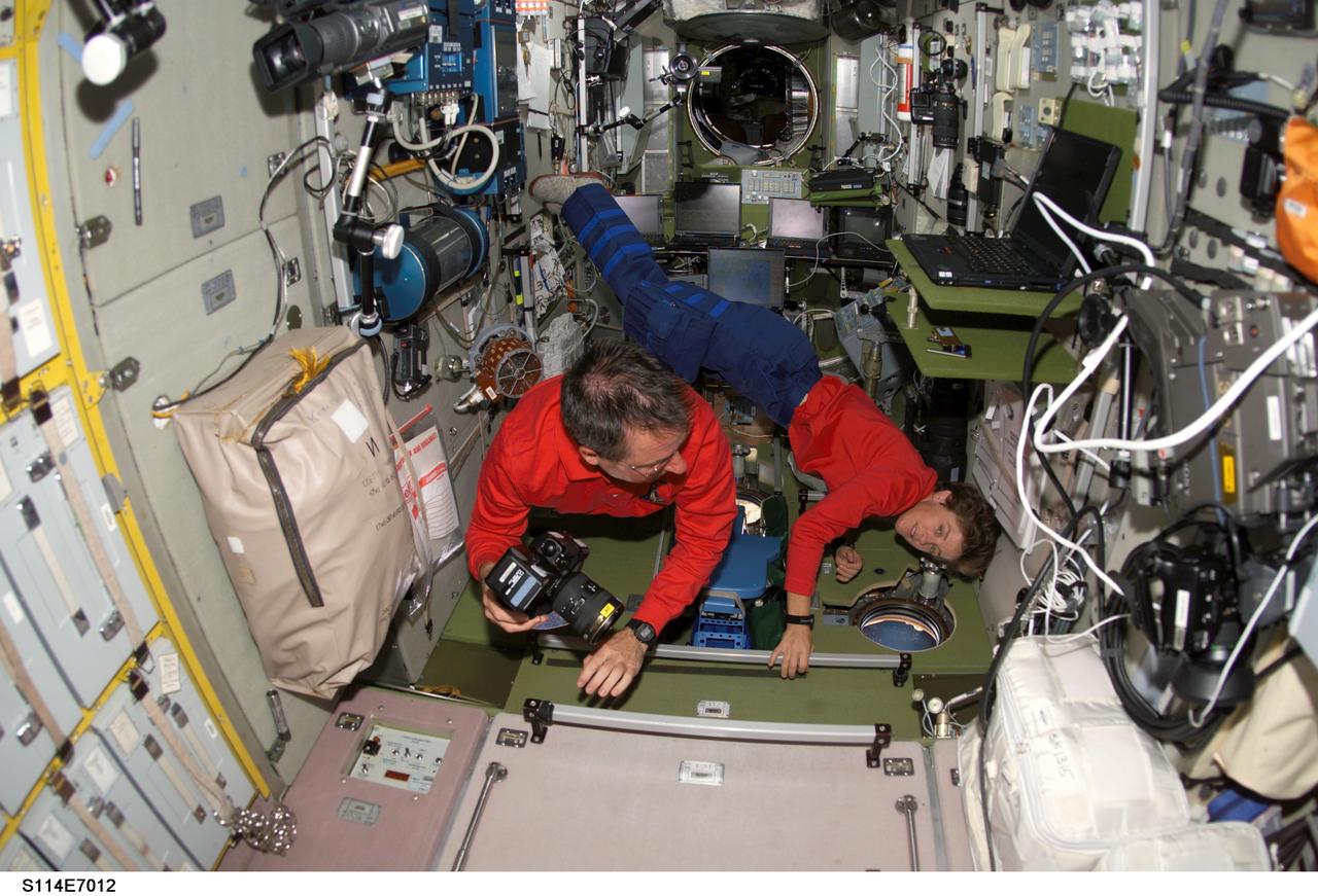 S114-E-7012 (4 August 2005) --- Astronaut Stephen K. Robinson (left), STS-114 mission specialist, holds a camera as he floats through the Zvezda Service Module of the International Space Station. Astronaut Wendy B. Lawrence, mission specialist, looks through a window at the Earth below.