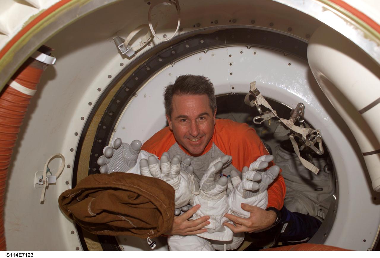 S114-E-7123 (5 August 2005) --- Astronaut Stephen K. Robinson, STS-114 mission specialist, holds Extravehicular Mobility Unit (EMU) spacesuit gloves as he floats through a hatch while Space Shuttle Discovery was docked to the International Space Station.
