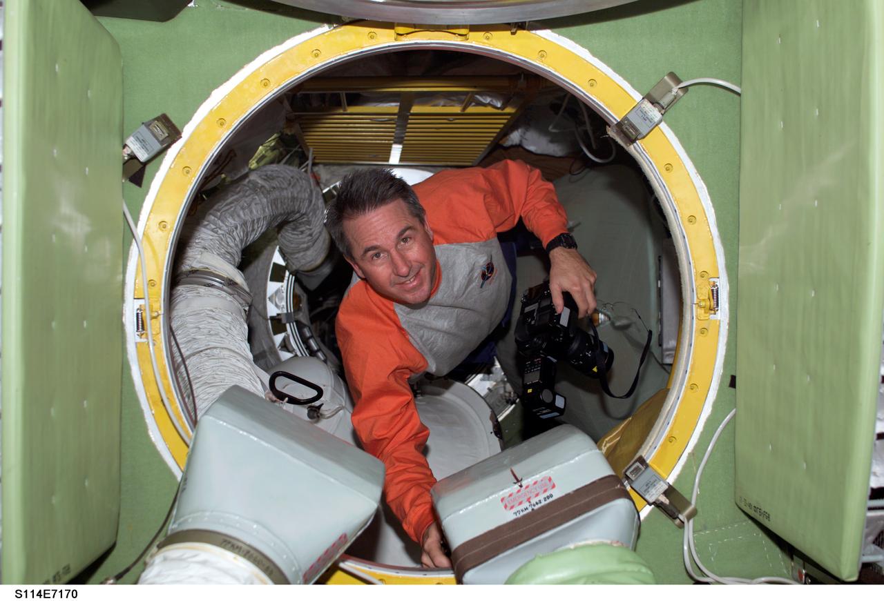 S114-E-7170 (5 August 2005) --- Astronaut Stephen K, Robinson, STS-114 mission specialist, holds a camera while floating through a hatch on the International Space Station. The crewmembers were making final preparations for Space Shuttle Discovery&#0146;s scheduled departure on August 6.