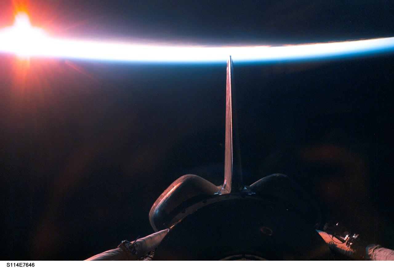 S114-E-7646 (6 August 2005) --- A sunrise dissecting a line of airglow of Earth's atmosphere provides the backdrop for this image featuring a portion of the Space Shuttle Discovery&#0146;s aft cargo bay, its vertical stabilizer and orbital maneuvering system (OMS) pods after departure from the International Space Station. The image was photographed by an STS-114 crewmember onboard the Shuttle.
