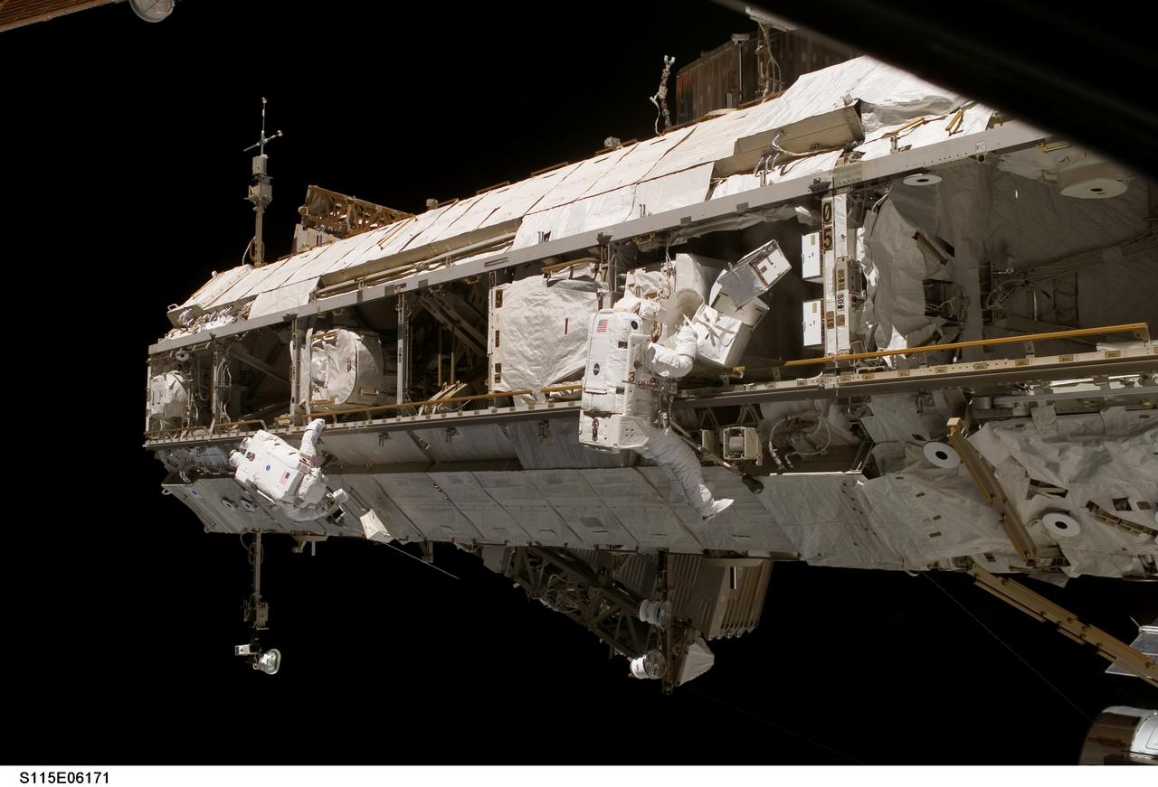 View of Astronaut Joseph R. (Joe) Tanner, STS-115 Mission Specialist (MS), in the red striped Extravehicular Mobility Unit (EMU), as he uses the Infrared (IR) CAM from the Forward (FWD) side of the S1 Truss to take image of the Starboard (STBD) Wing Leading Edge (WLE) of Atlantis for Detailed Test Objective (DTO) 851 while Astronaut Heidemarie M. Stefanyshyn-Piper, STS-115 MS, in the white striped EMU, removes stowed equipment during third Extravehicular Activity (EVA).
