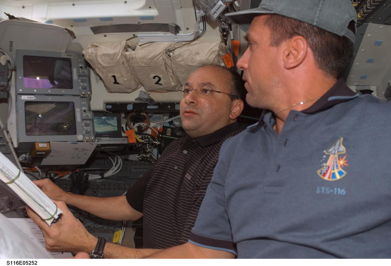 S116-E-05252 (10 Dec. 2006) --- Astronauts Mark L. Polansky (background) and William A. (Bill) Oefelein, STS-116 commander and pilot, respectively, look over procedures checklists on the flight deck of Space Shuttle Discovery during flight day two activities.