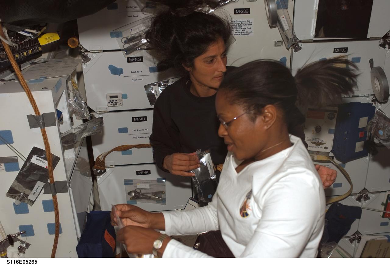 S116-E-05265 (10 Dec. 2006) --- Astronauts Joan E. Higginbotham (foreground) and Sunita L. Williams, both STS-116 mission specialists, prepare to eat a meal on the middeck of Space Shuttle Discovery. Williams will join the Expedition 14 crew as flight engineer after she enters the International Space Station. Docking of the two spacecraft will occur on Dec. 11.
