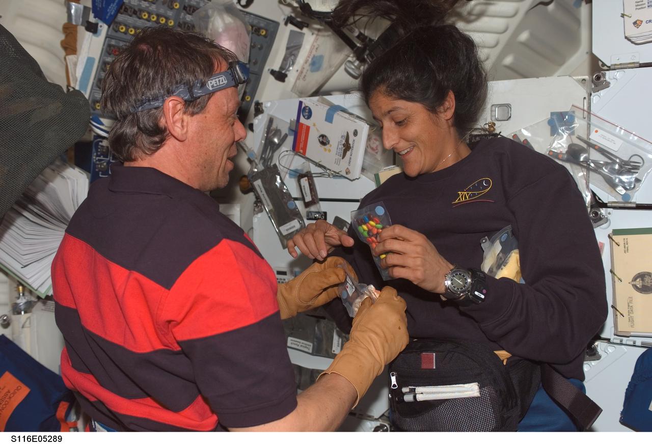 S116-E-05289 (10 Dec. 2006) --- Astronaut Sunita L. Williams (right) and European Space Agency (ESA) astronaut Christer Fuglesang, both STS-116 mission specialists, enjoy a light moment as they prepare to open food packages on the middeck of Space Shuttle Discovery. Williams will join the Expedition 14 crew as flight engineer after she enters the International Space Station. Docking of the two spacecraft will occur on Dec. 11.