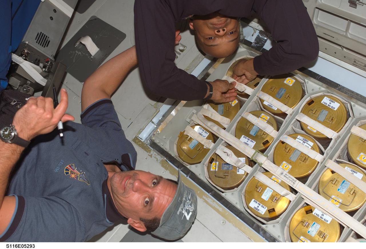 S116-E-05293 (10 Dec. 2006) --- Astronauts William A. (Bill) Oefelein (bottom) and Robert L. Curbeam, Jr., STS-116 pilot and mission specialist, respectively, work with the lithium hydroxide (LiOH) canisters beneath Space Shuttle Discovery's middeck.