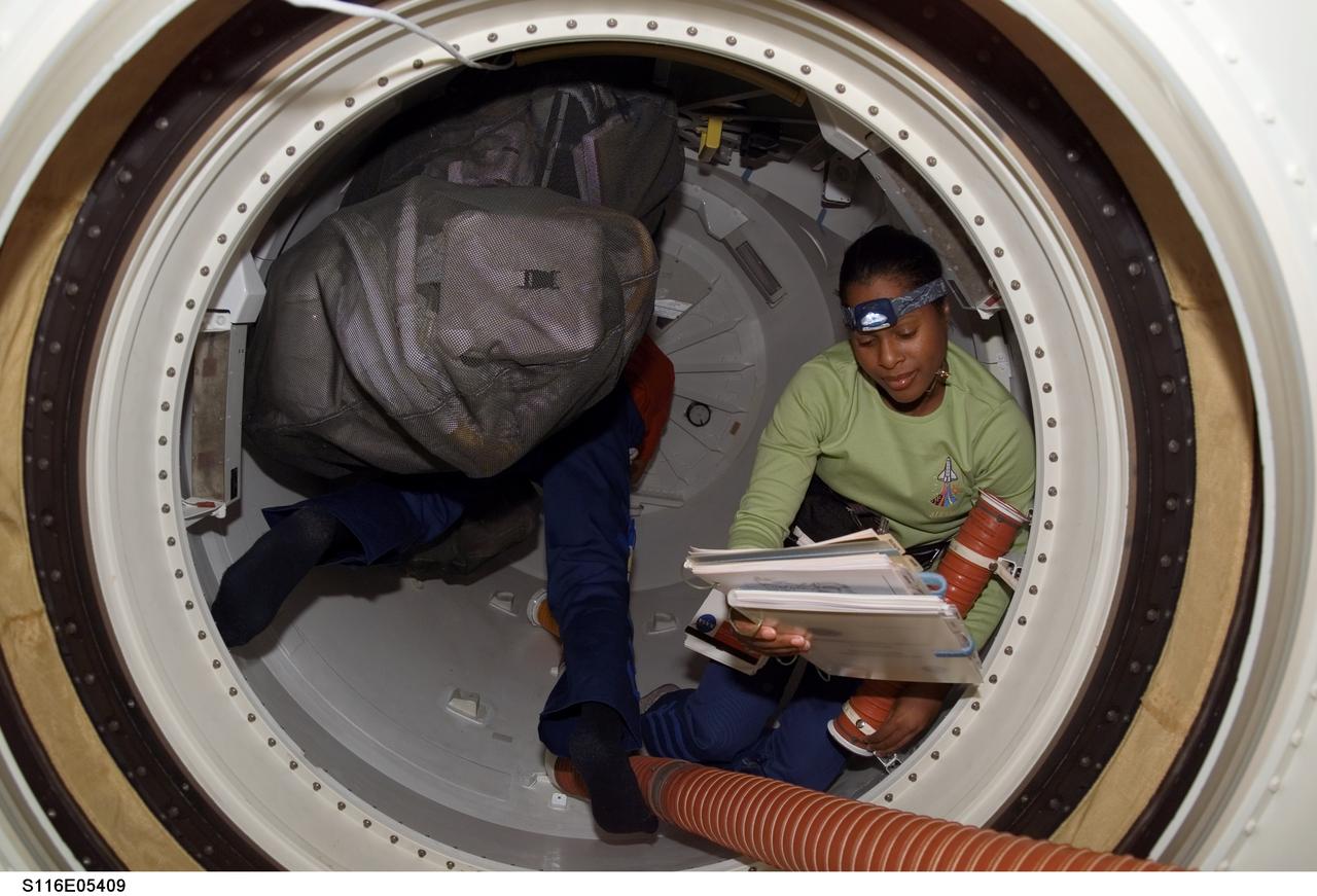 S116-E-05409 (11 Dec. 2006) --- Astronaut Joan E. Higginbotham, STS-116 mission specialist, looks over procedures checklists in a hatch on Space Shuttle Discovery during flight day three activities.