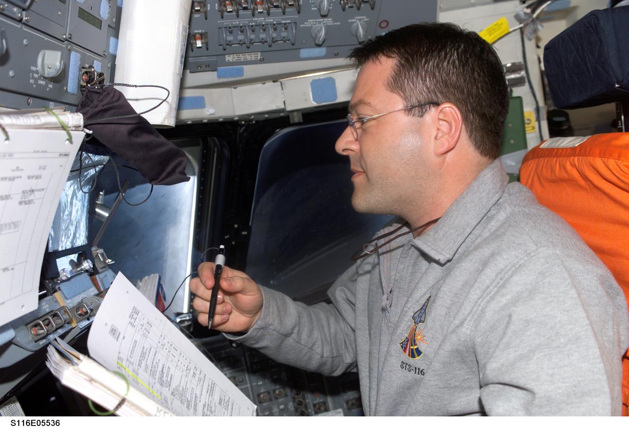 S116-E-05536 (11 Dec. 2006) --- Astronaut Nicholas J. M. Patrick, STS-116 mission specialist, looks over procedures checklists on the aft flight deck of Space Shuttle Discovery during flight day three activities.