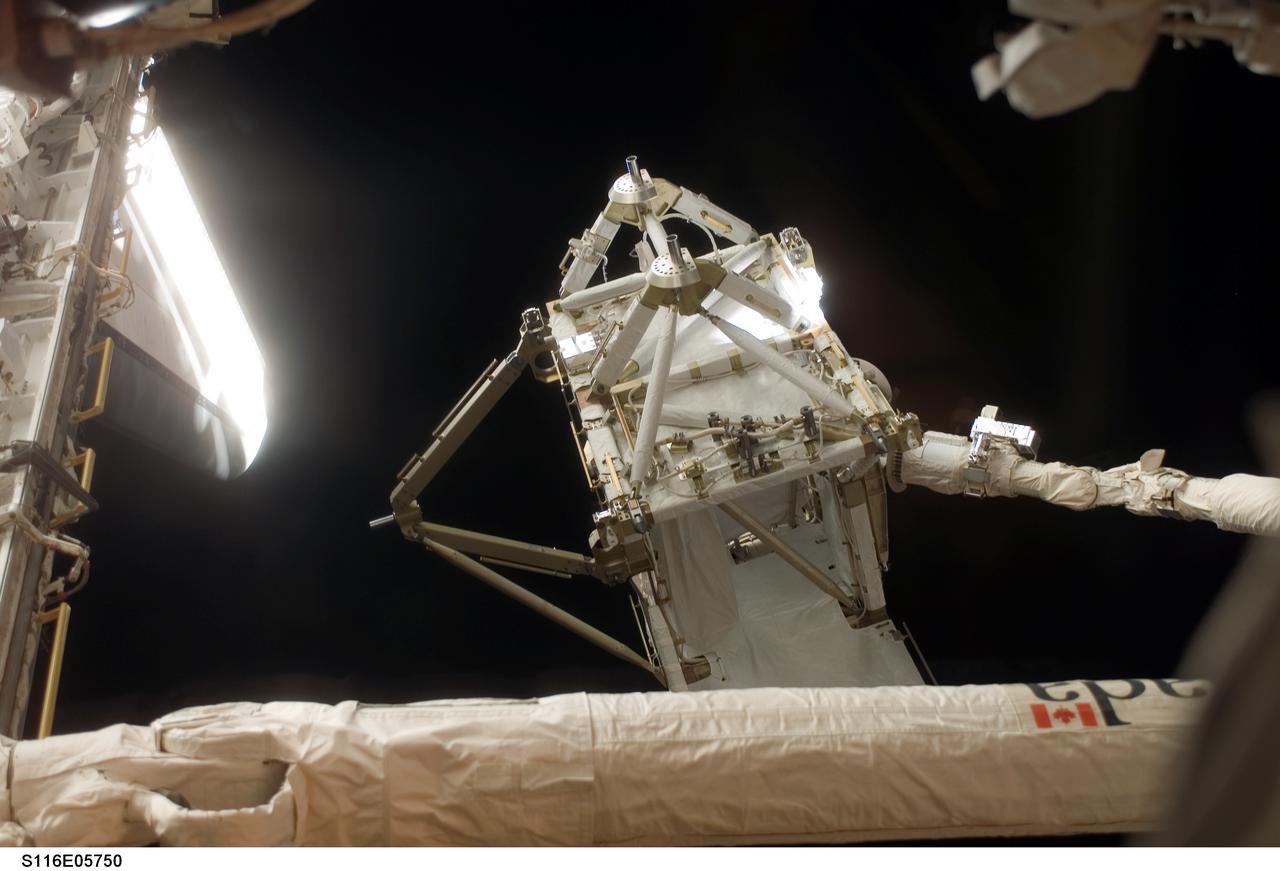 S116-E-05750 (11 Dec. 2006) --- The International Space Station's new P5 truss section is moved out of Space Shuttle Discovery's payload bay by a cabin-bound STS-116 crewmember, using the shuttle's Remote Manipulator System (RMS) robotic arm. The truss section will be handed to the station's Canadarm2 and will remain suspended over Discovery's port wing overnight, awaiting installation in the first of three planned spacewalks on Dec. 12.