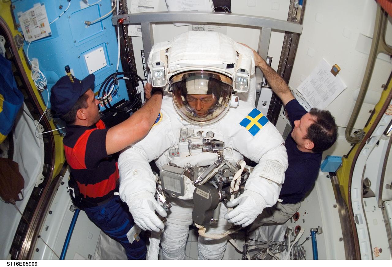 S116-E-05909 (12 Dec. 2006) --- As the mission's first spacewalk draws to a close, astronauts William A. (Bill) Oefelein (left), STS-116 pilot, and Michael E. Lopez-Alegria, Expedition 14 commander and NASA space station science officer, assist European Space Agency (ESA) astronaut Christer Fuglesang, STS-116 mission specialist, as he removes his extravehicular mobility unit (EMU) spacesuit in the Quest Airlock of the International Space Station.