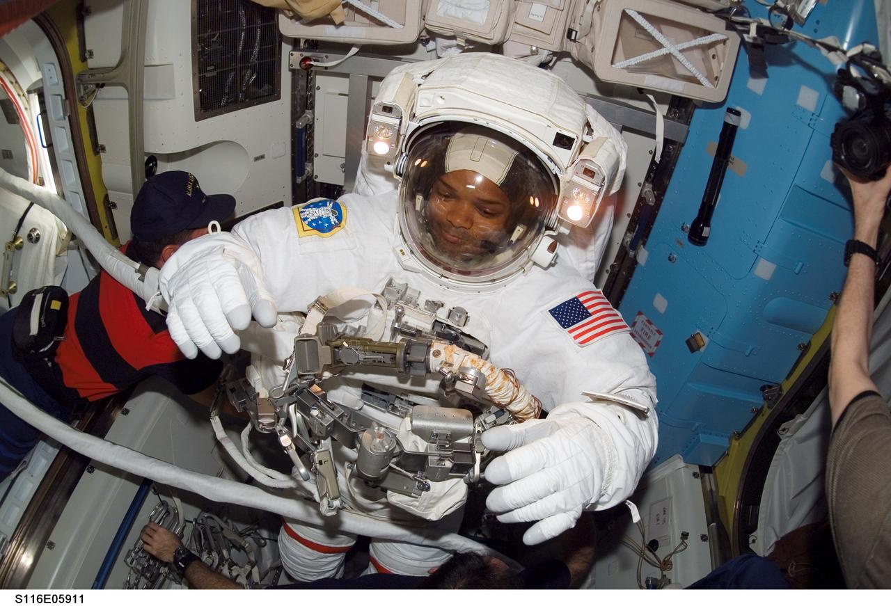 S116-E-05911 (12 Dec. 2006) --- As the mission's first spacewalk draws to a close, astronaut Robert L. Curbeam, Jr., STS-116 mission specialist, gets helps as he removes his extravehicular mobility unit (EMU) spacesuit in the Quest Airlock of the International Space Station. Astronaut William A. (Bill) Oefelein (left), pilot, assisted Curbeam.