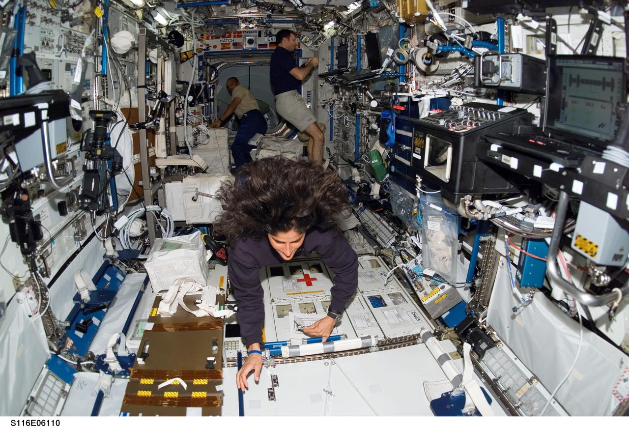 S116-E-06110 (13 Dec. 2006) --- Astronaut Sunita L. Williams, Expedition 14 flight engineer, works in the Destiny laboratory of the International Space Station. Astronauts Robert L. Curbeam, Jr., STS-116 mission specialist, and Michael E. Lopez-Alegria, Expedition 14 commander and NASA space station science officer, are visible in the background.