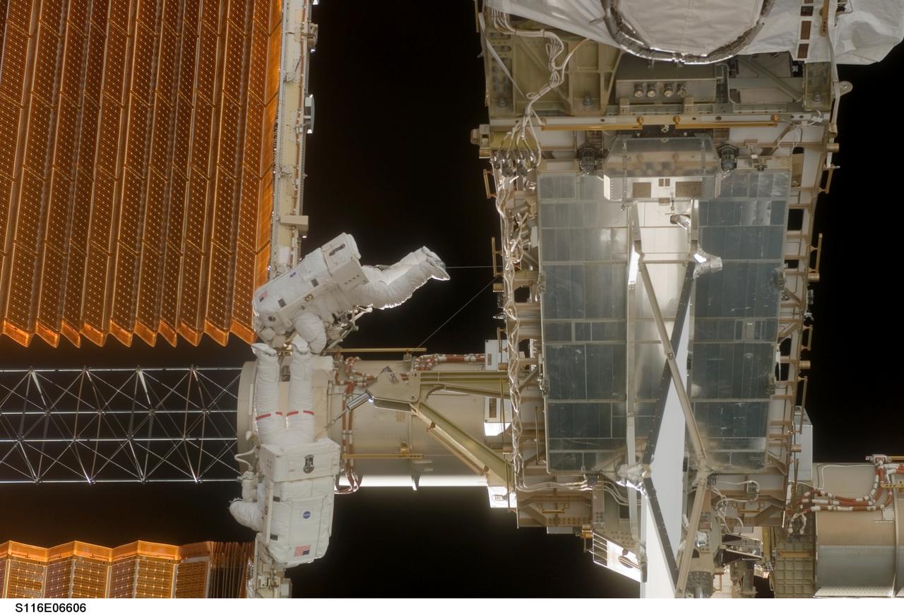 S116-E-06606 (16 Dec. 2006) --- Astronauts Robert L. Curbeam, Jr., (red stripes), STS-116 mission specialist, and Sunita L. Williams, Expedition 14 flight engineer, work near the International Space Station's left P6 solar array wing during the mission's third planned session of extravehicular activity (EVA) as construction resumes on the International Space Station.