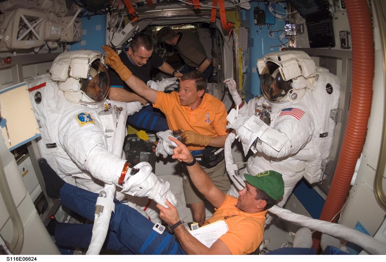 S116-E-06624 (16 Dec. 2006) --- As the mission's third spacewalk draws to a close, astronauts Robert L. Curbeam, Jr. (left), STS-116 mission specialist, and Sunita L. Williams, Expedition 14 flight engineer, get help as they remove their extravehicular mobility unit (EMU) spacesuits in the Quest Airlock of the International Space Station. Astronaut William A. (Bill) Oefelein (bottom), pilot; European Space Agency (ESA) astronaut Christer Fuglesang, mission specialist; and cosmonaut Mikhail Tyurin, Expedition 14 flight engineer representing Russia's Federal Space Agency, assisted Curbeam and Williams.