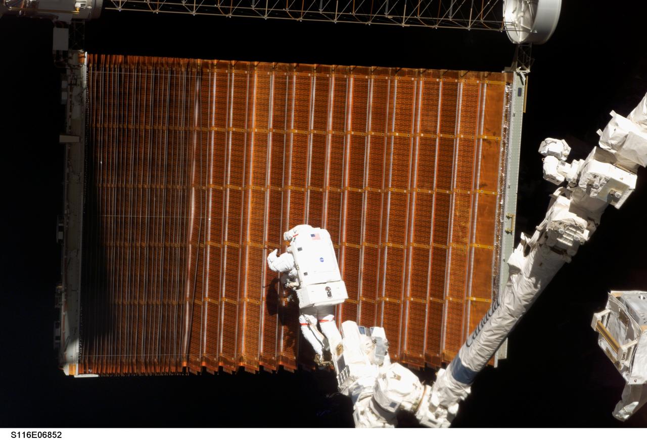 S116-E-06852 (18 Dec. 2006) --- Anchored to the International Space Station's Canadarm2 foot restraint, astronaut Robert L. Curbeam Jr., STS-116 mission specialist, works with the port overhead solar array wing on the International Space Station's P6 truss during the mission's fourth session of extravehicular activity (EVA). European Space Agency (ESA) astronaut Christer Fuglesang (out of frame), mission specialist, worked in tandem with Curbeam, using specially-prepared, tape-insulated tools, to guide the array wing neatly inside its blanket box during the 6-hour, 38-minute spacewalk.