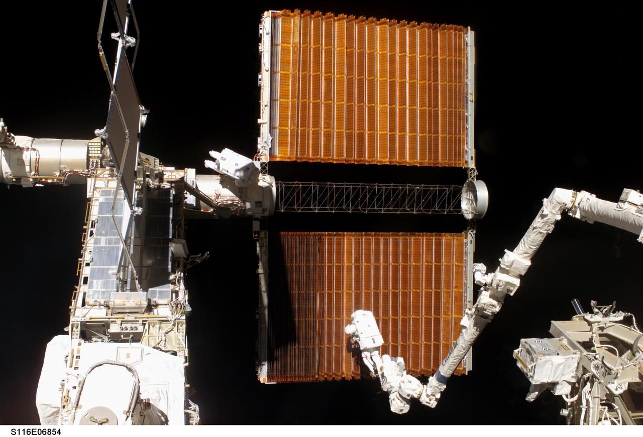 S116-E-06854 (18 Dec. 2006) --- Anchored to the International Space Station's Canadarm2 foot restraint, astronaut Robert L. Curbeam Jr. and European Space Agency (ESA) astronaut Christer Fuglesang (center), both STS-116 mission specialists, work with the port overhead solar array wing on the station's P6 truss during the mission's fourth session of extravehicular activity (EVA). The spacewalkers used specially-prepared, tape-insulated tools, to guide the array wing neatly inside its blanket box during the 6-hour, 38-minute spacewalk.