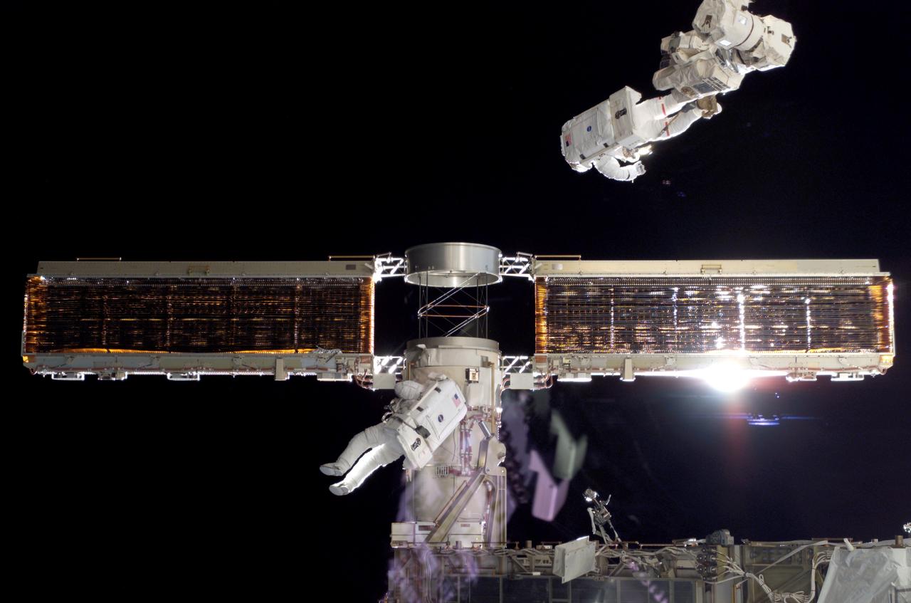 S116-E-06858 (18 Dec. 2006) --- Anchored to the International Space Station's Canadarm2 foot restraint, astronaut Robert L. Curbeam Jr. (top) and European Space Agency (ESA) astronaut Christer Fuglesang (center), both STS-116 mission specialists, work with the port overhead solar array wing on the station's P6 truss during the mission's fourth session of extravehicular activity (EVA). The spacewalkers used specially-prepared, tape-insulated tools, to guide the array wing neatly inside its blanket box during the 6-hour, 38-minute spacewalk.