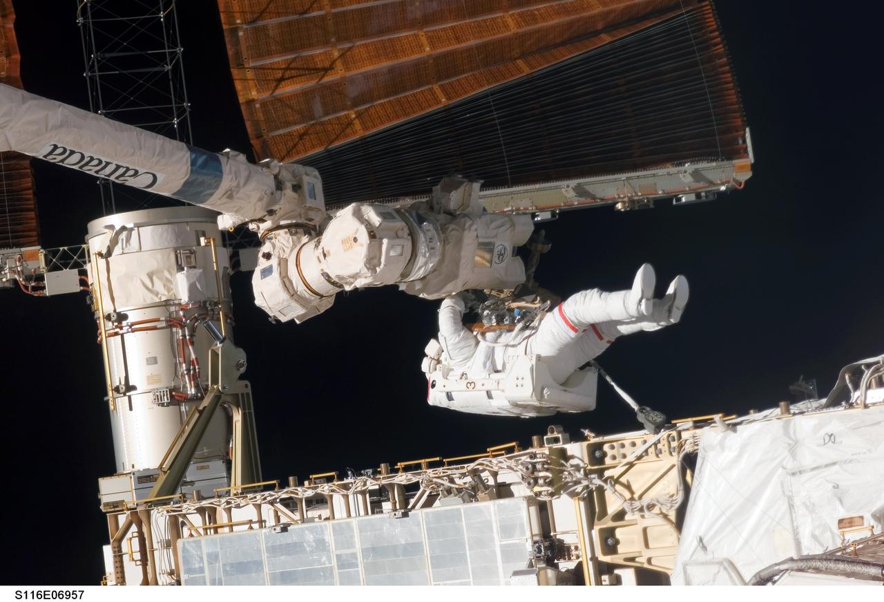 S116-E-06957 (18 Dec. 2006) --- Astronaut Robert L. Curbeam Jr., STS-116 mission specialist, works with the port overhead solar array wing on the International Space Station's P6 truss during the mission's fourth session of extravehicular activity (EVA). European Space Agency (ESA) astronaut Christer Fuglesang (out of frame), mission specialist, worked in tandem with Curbeam, using specially-prepared, tape-insulated tools, to guide the array wing neatly inside its blanket box during the 6-hour, 38-minute spacewalk.