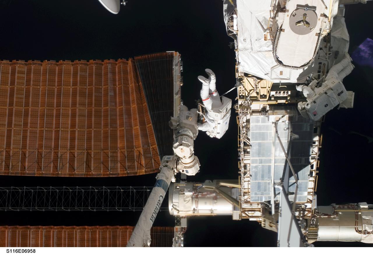 S116-E-06958 (18 Dec. 2006) --- Astronaut Robert L. Curbeam Jr. (center) and European Space Agency (ESA) astronaut Christer Fuglesang (right), both STS-116 mission specialists, work with the port overhead solar array wing on the International Space Station's P6 truss during the mission's fourth session of extravehicular activity (EVA). The spacewalkers used specially-prepared, tape-insulated tools, to guide the array wing neatly inside its blanket box during the 6-hour, 38-minute spacewalk.