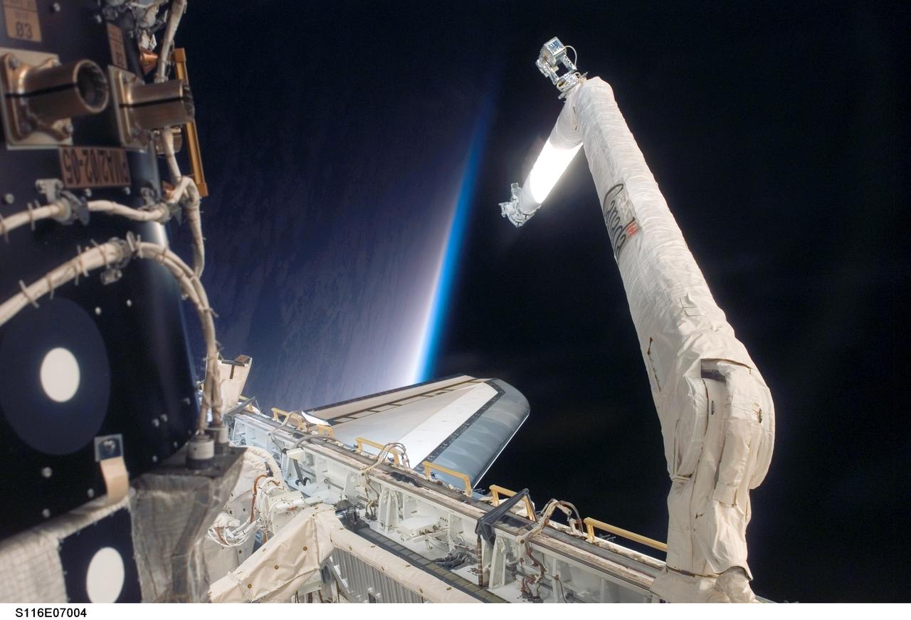 S116-E-07004 (18 Dec. 2006) --- As seen through windows on the aft flight deck of Space Shuttle Discovery, the Remote Manipulator System (RMS) is featured in this image photographed by a STS-116 crewmember during flight day ten activities while Discovery was docked with the International Space Station. The blackness of space, Earth's horizon and airglow provide the backdrop for the scene.