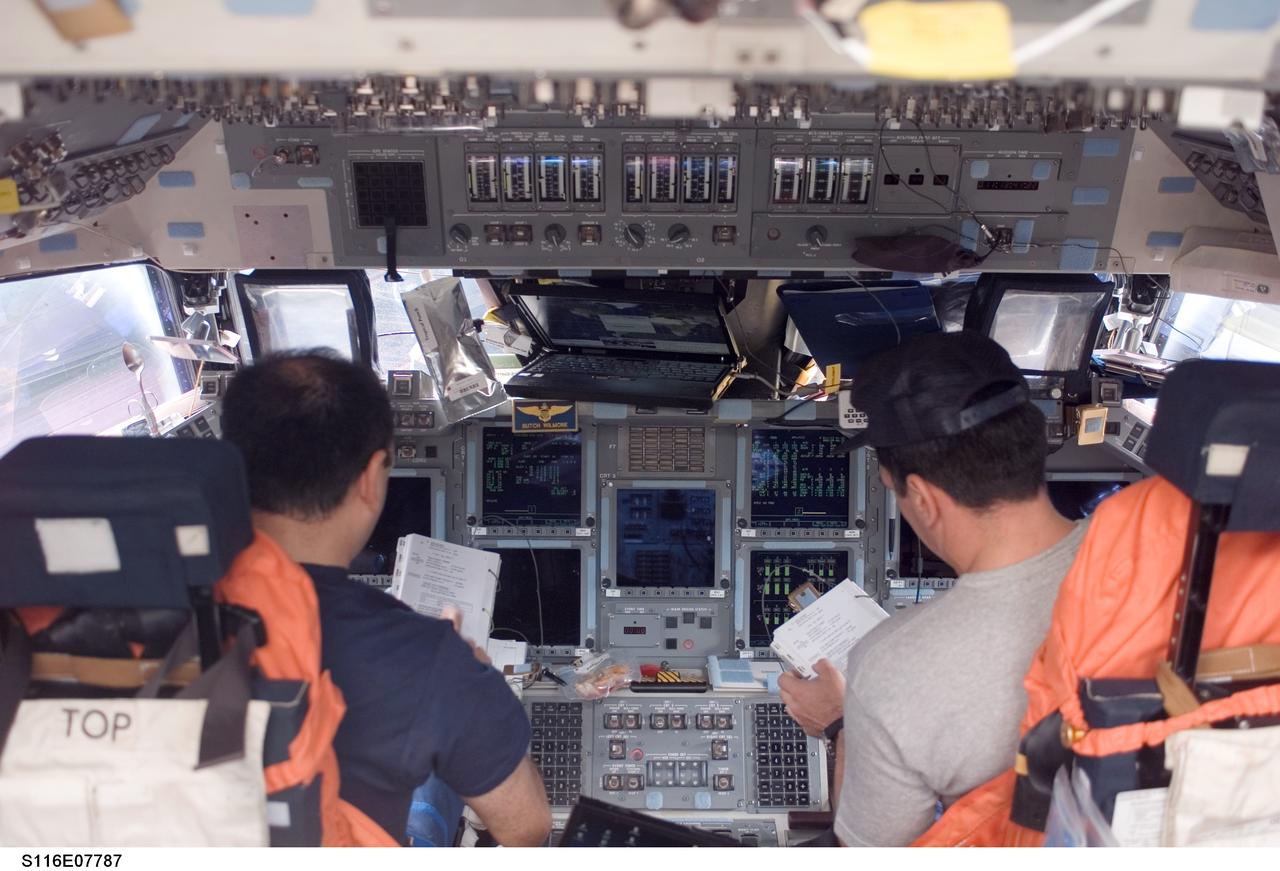 S116-E-07787 (21 Dec. 2006) --- Astronauts Mark L. Polansky (left) and William A. (Bill) Oefelein, STS-116 commander and pilot, respectively, look over procedures checklists on the forward flight deck of Space Shuttle Discovery during flight day 13 activities.
