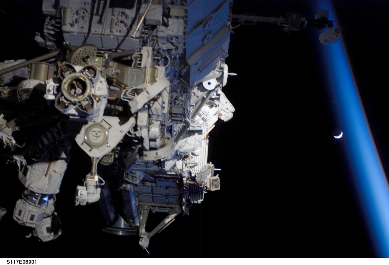 S117-E-06901 (11 June 2007) --- Astronauts Jim Reilly (out of frame) and John "Danny" Olivas (partially obscured, center), both STS-117 mission specialists, participate in the mission's first planned session of extravehicular activity (EVA), as construction resumes on the International Space Station. Among other tasks, Reilly and Olivas connected power, data and cooling cables between S1 and S3; released the launch restraints from and deployed the four solar array blanket boxes on S4 and released the cinches and winches holding the photovoltaic radiator on S4. Earth's horizon and a crescent moon are visible at right.