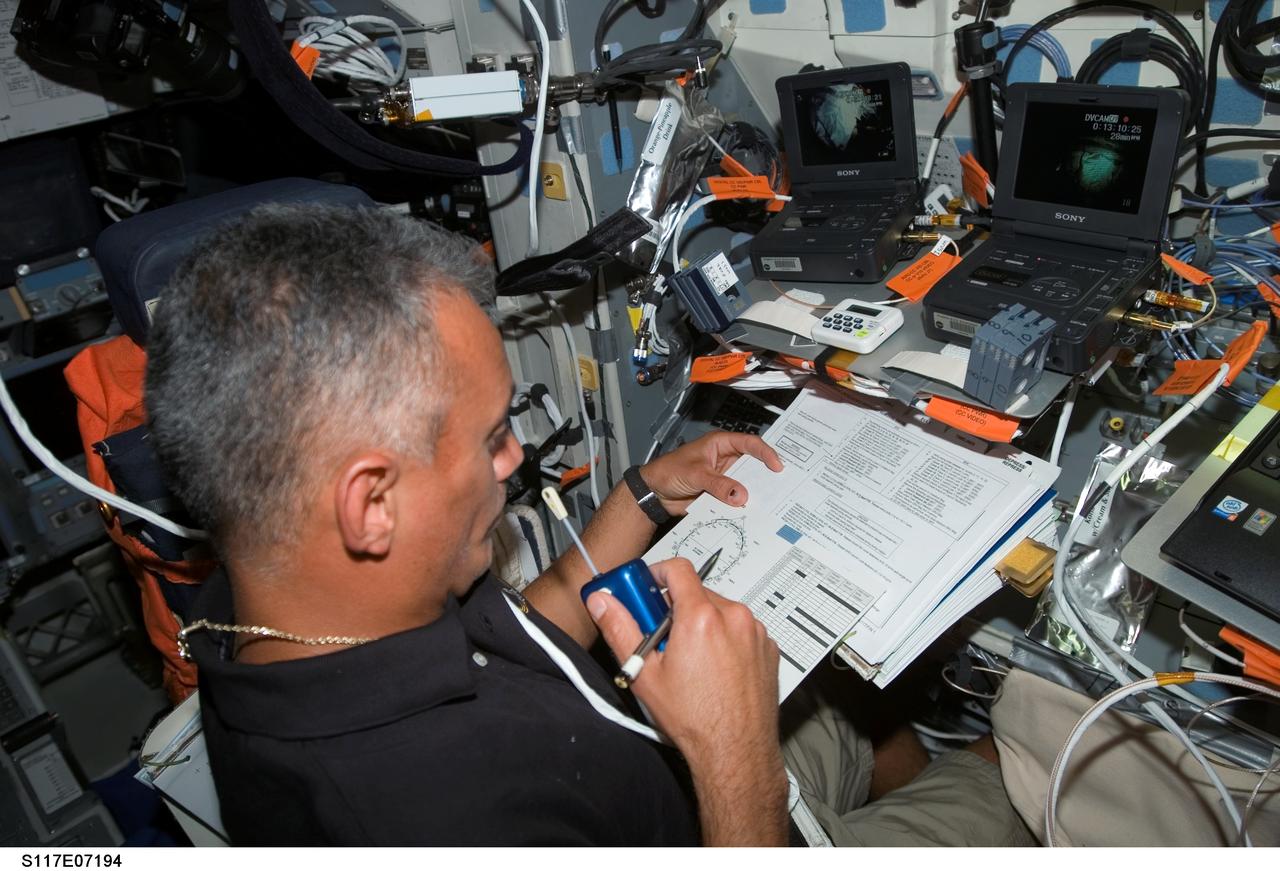 S117-E-07194 (13 June 2007) --- Astronaut John "Danny" Olivas, STS-117 mission specialist, uses a communication system while looking over procedures checklists on the flight deck of Space Shuttle Atlantis during flight day six activities while docked with the International Space Station.