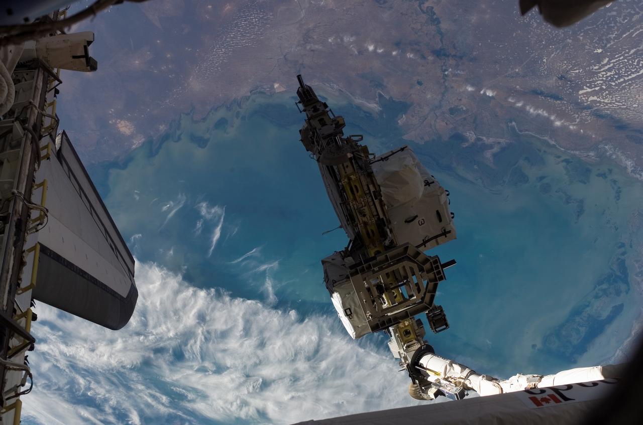 S118-E-07111 (14 Aug. 2007) --- Backdropped by a colorful Earth, the Space Shuttle Endeavour's Remote Manipulator System (RMS) robotic arm moves an external stowage platform (ESP-3) for a hand-off to the station's robotic arm (out of frame) while docked with the International Space Station. Astronauts Tracy Caldwell and Barbara R. Morgan, both STS-118 mission specialists, were inside at Endeavour's controls as the shuttle's robotic arm lifted the storage platform from the cargo bay to hand it over to the station's robotic arm, also known as Canadarm2. Astronauts Charlie Hobaugh, pilot, and Clay Anderson, Expedition 15 flight engineer, then used Canadarm2 to attach the 13-by-7-foot platform to the station's Port 3 truss.