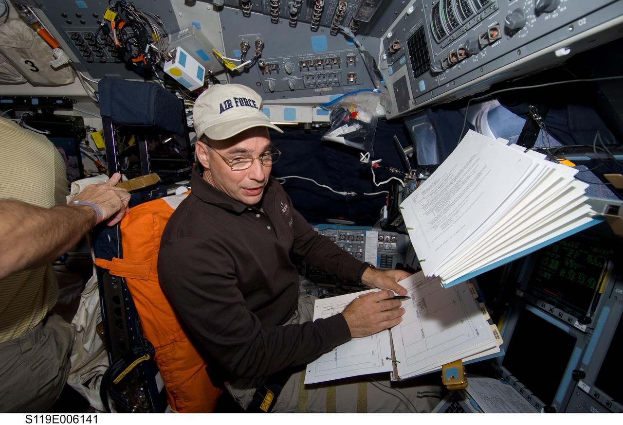 S119-E-006141 (16 March 2009) --- Astronaut Lee Archambault, STS-119 commander, looks over checklists while occupying the commander’s station on the flight deck of Space Shuttle Discovery during flight day two activities.